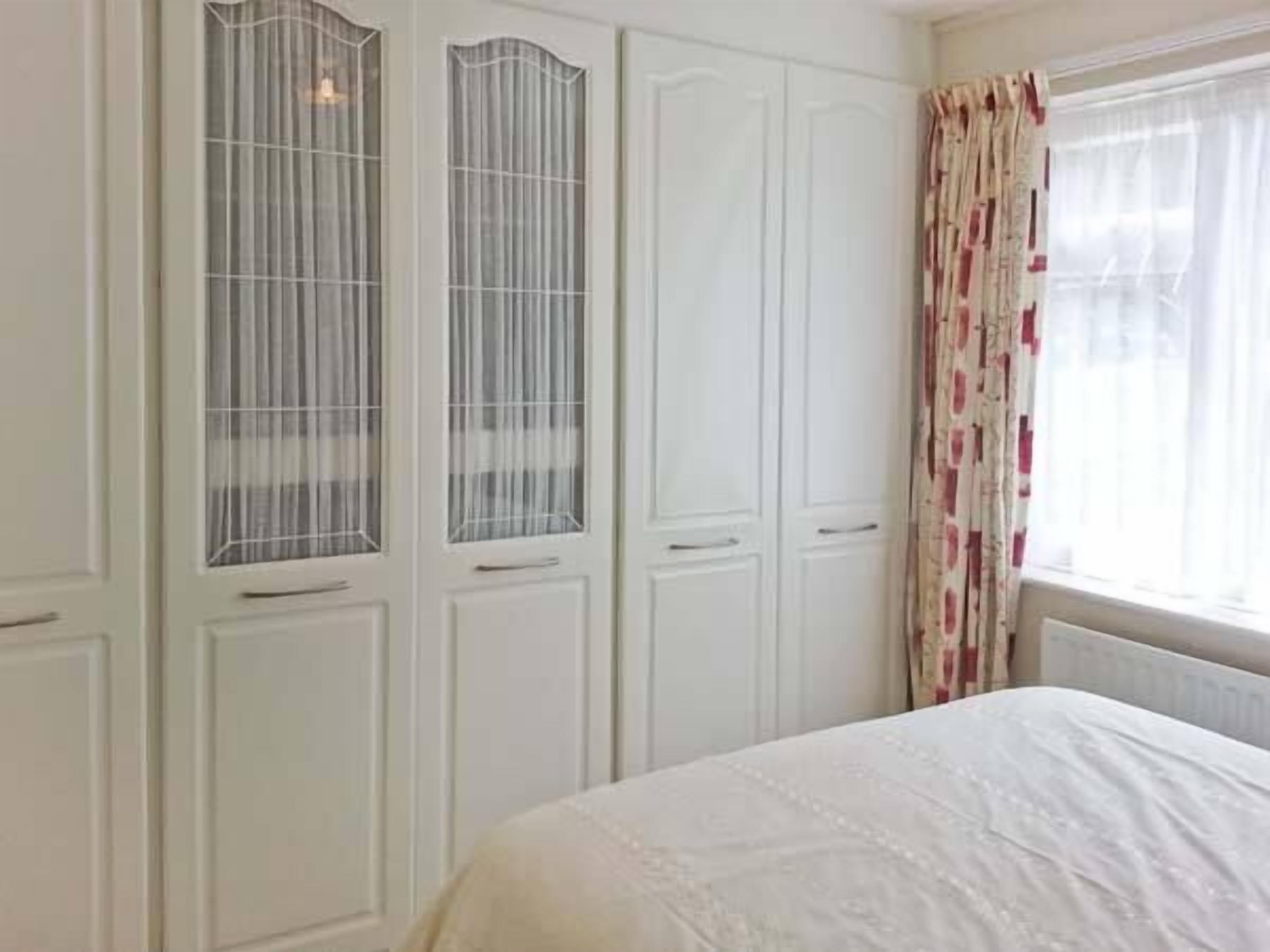 A bedroom with a bed, white wardrobe, and a window with curtains.