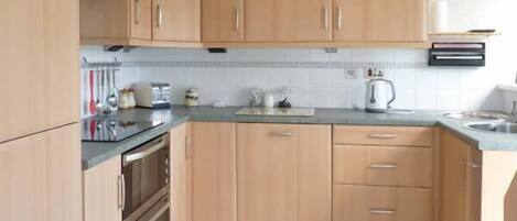 A kitchen with wooden cabinets, a countertop, a kettle, and a sink.