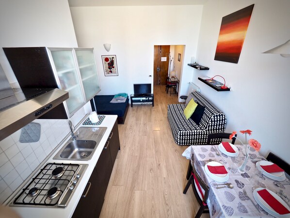 A compact kitchen with a stove, sink, and a dining area with a table set for two. - Dimora Palestro con Panorama (Genoa)