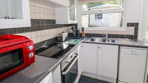 Une cuisine de taille réduite avec des meubles blancs, un micro-ondes rouge, un évier et une fenêtre.