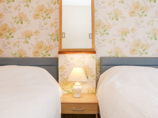 A hotel room with floral wallpaper, two beds, a nightstand with a lamp, and a framed picture on the wall.