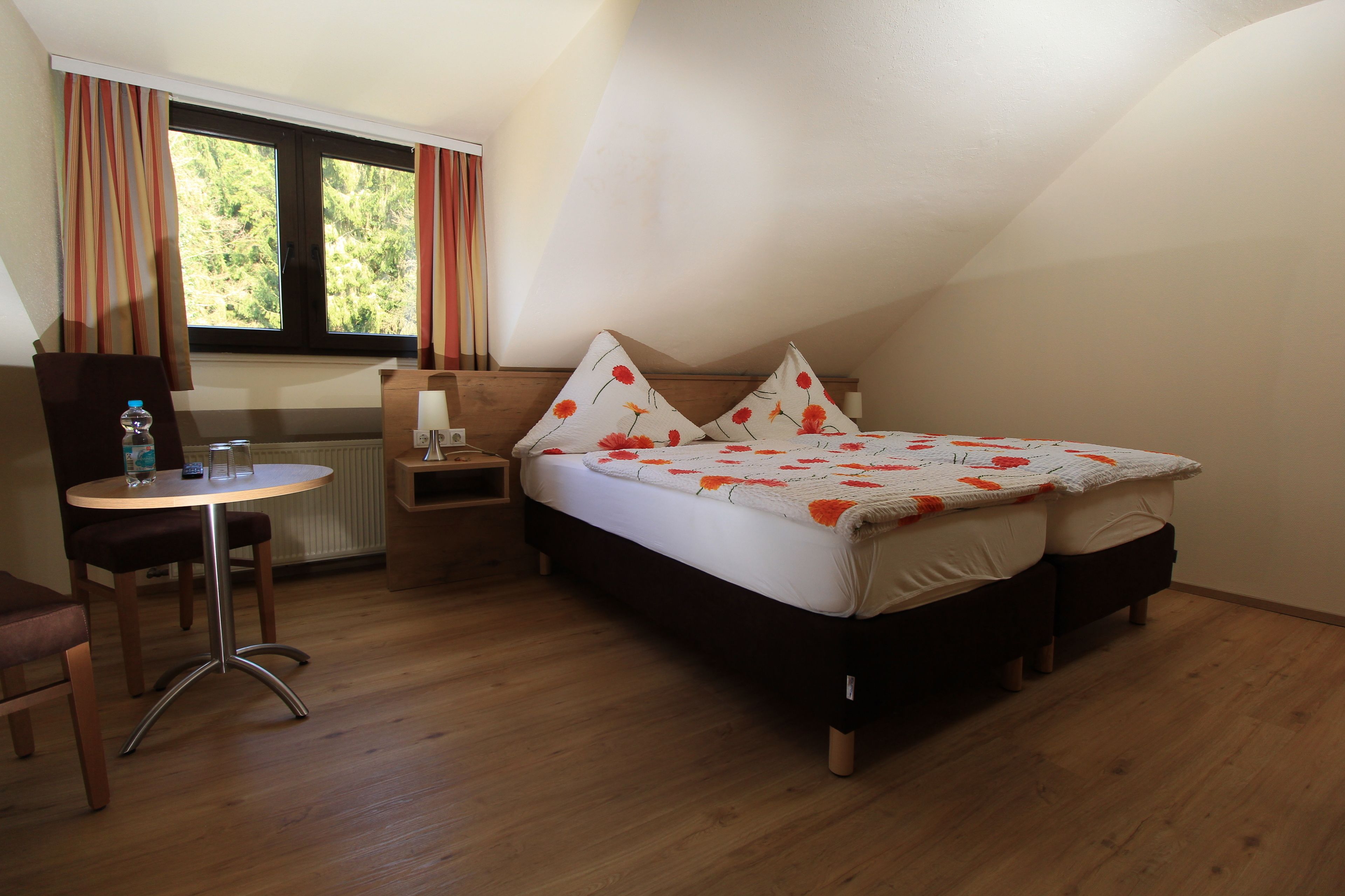 A bedroom with a bed, bedside table, chair, and a window with curtains.