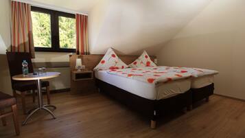 A bedroom with a bed, bedside table, chair, and a window with curtains.