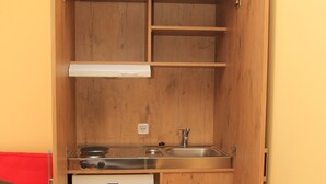 Une petite cuisine équipée, avec une cuisinière, un évier et un réfrigérateur intégrés, située à côté d’un canapé rouge.