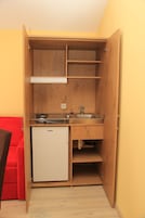 A compact kitchenette with a built-in stove, sink, and refrigerator, adjacent to a red sofa.