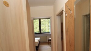Un couloir étroit, doté d’un plancher en bois, mène à une chambre avec une fenêtre.