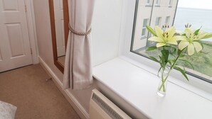 Une pièce avec un rebord de fenêtre, un radiateur blanc et un vase rempli de fleurs.