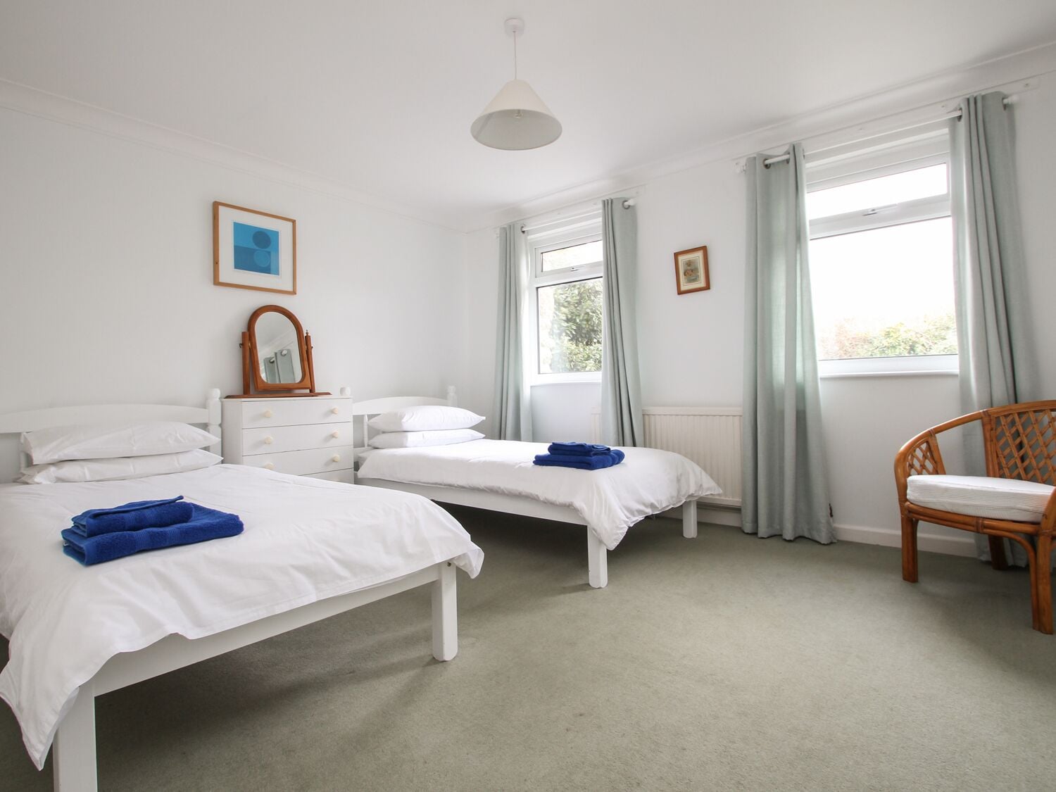 A bedroom with two beds, a chair, and a window with curtains.