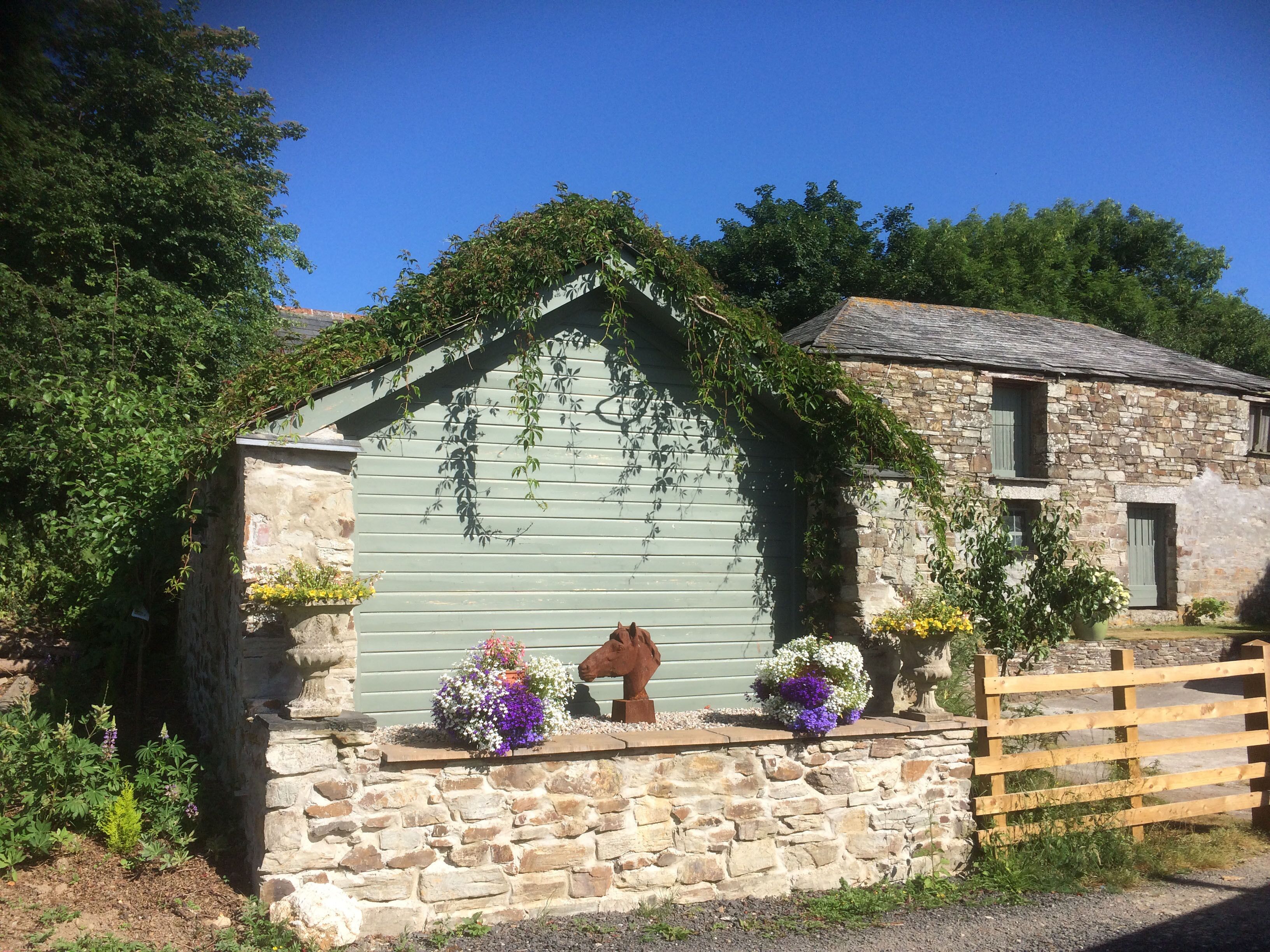 A stone building with a green roof, surrounded by lush greenery and a wooden fence.