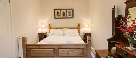 Una cama bien hecha con dos mesitas de noche, un cuadro enmarcado sobre la cama, un aparador de madera con un espejo y un libro encima.