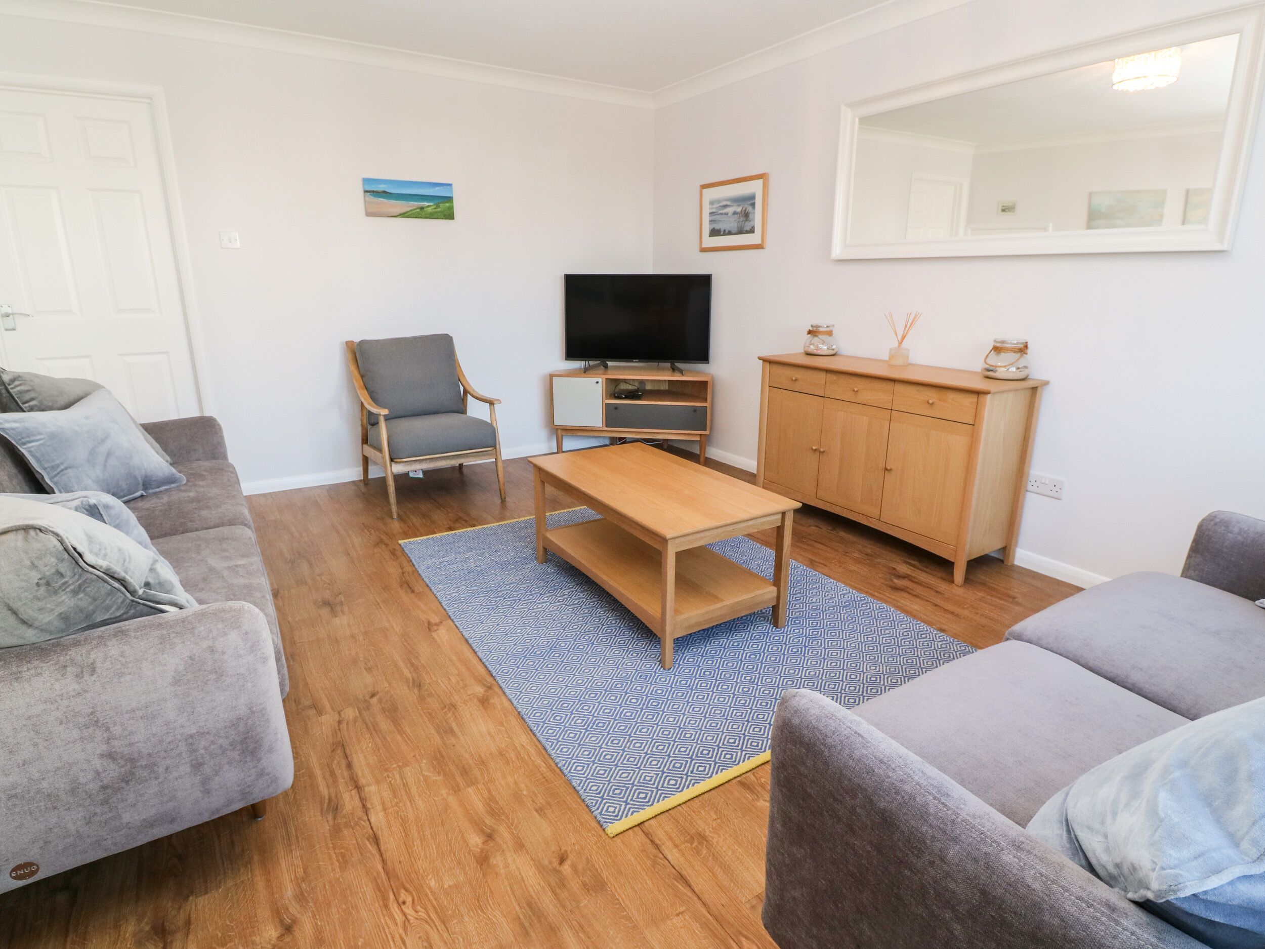 Een woonkamer met een grijze bank, een houten salontafel, een grijze fauteuil, een televisie en een houten kast.