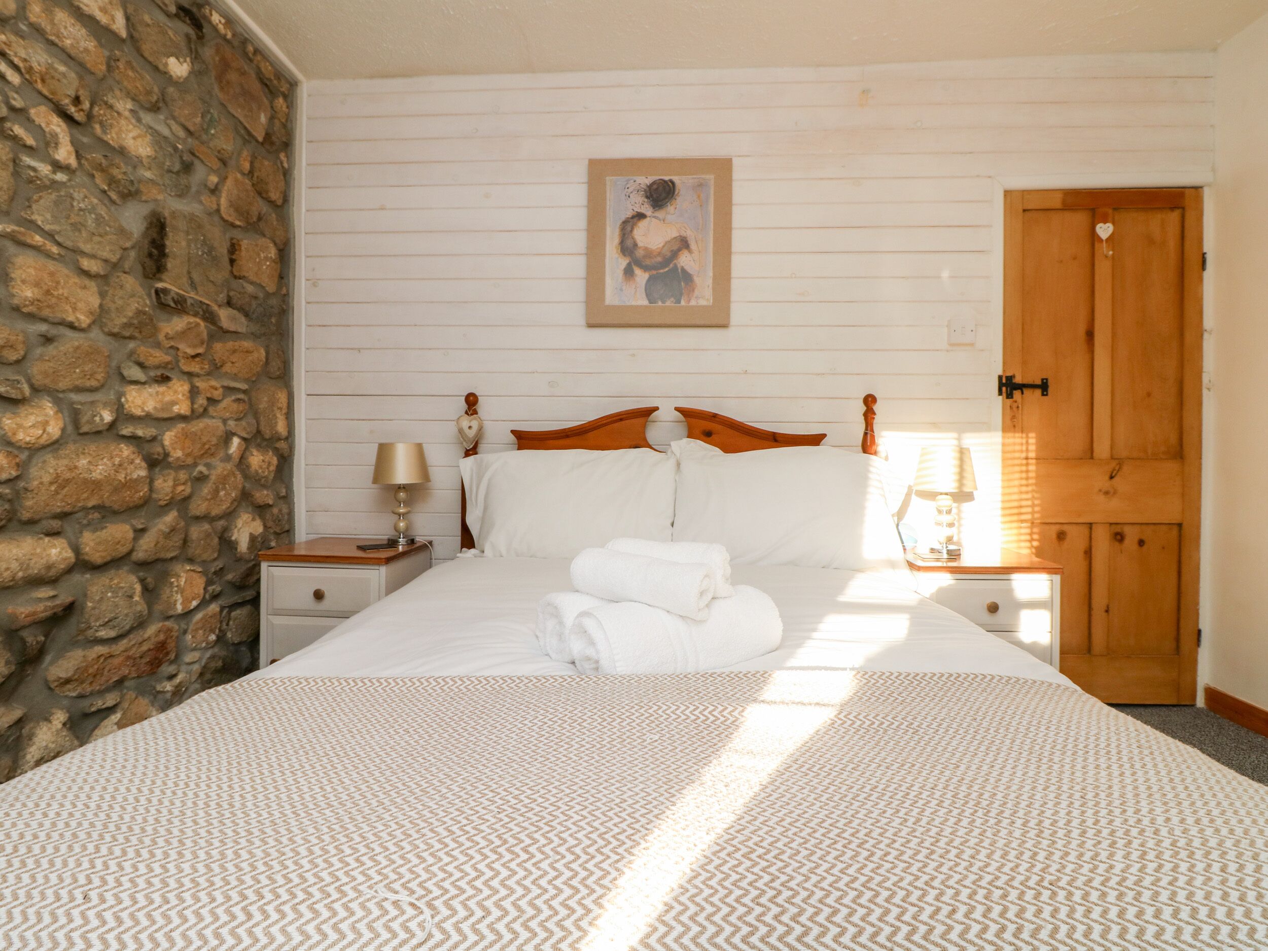 Une chambre avec un mur en pierre, un cadre de lit en bois, du linge de lit blanc et une porte en bois.