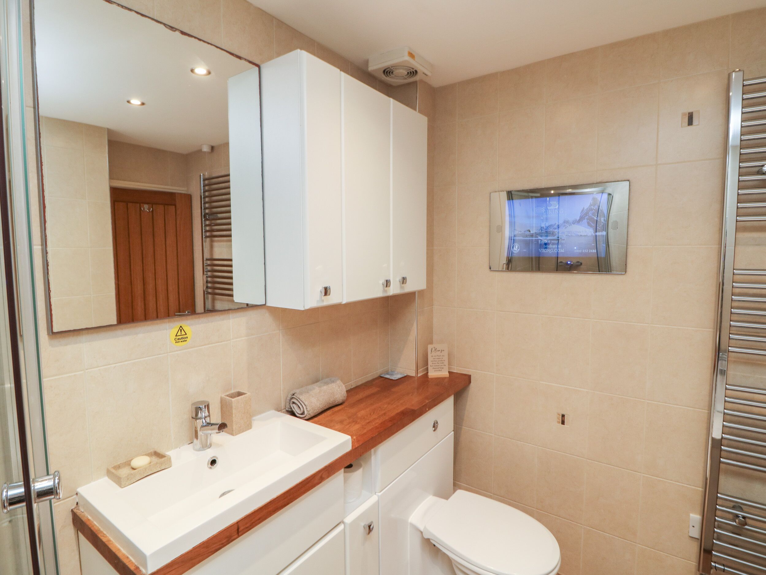 A bathroom with a white sink, wooden countertop, and a white toilet. There is a mirror above the sink and a towel rack on the wall.