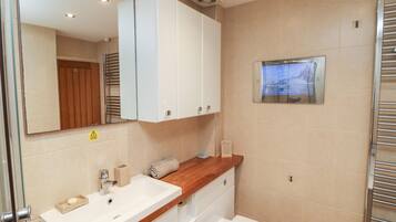 A bathroom with a white sink, wooden countertop, and a white toilet. There is a mirror above the sink and a towel rack on the wall.
