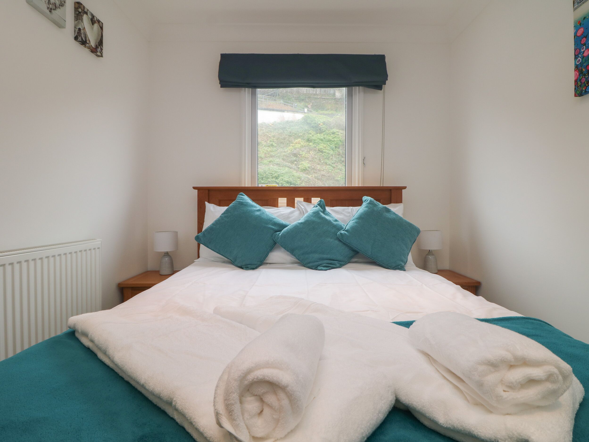 Una cama bien tendida con ropa de cama azul aguamarina y blanca, un cabecero de madera y una ventana con vistas a follaje.