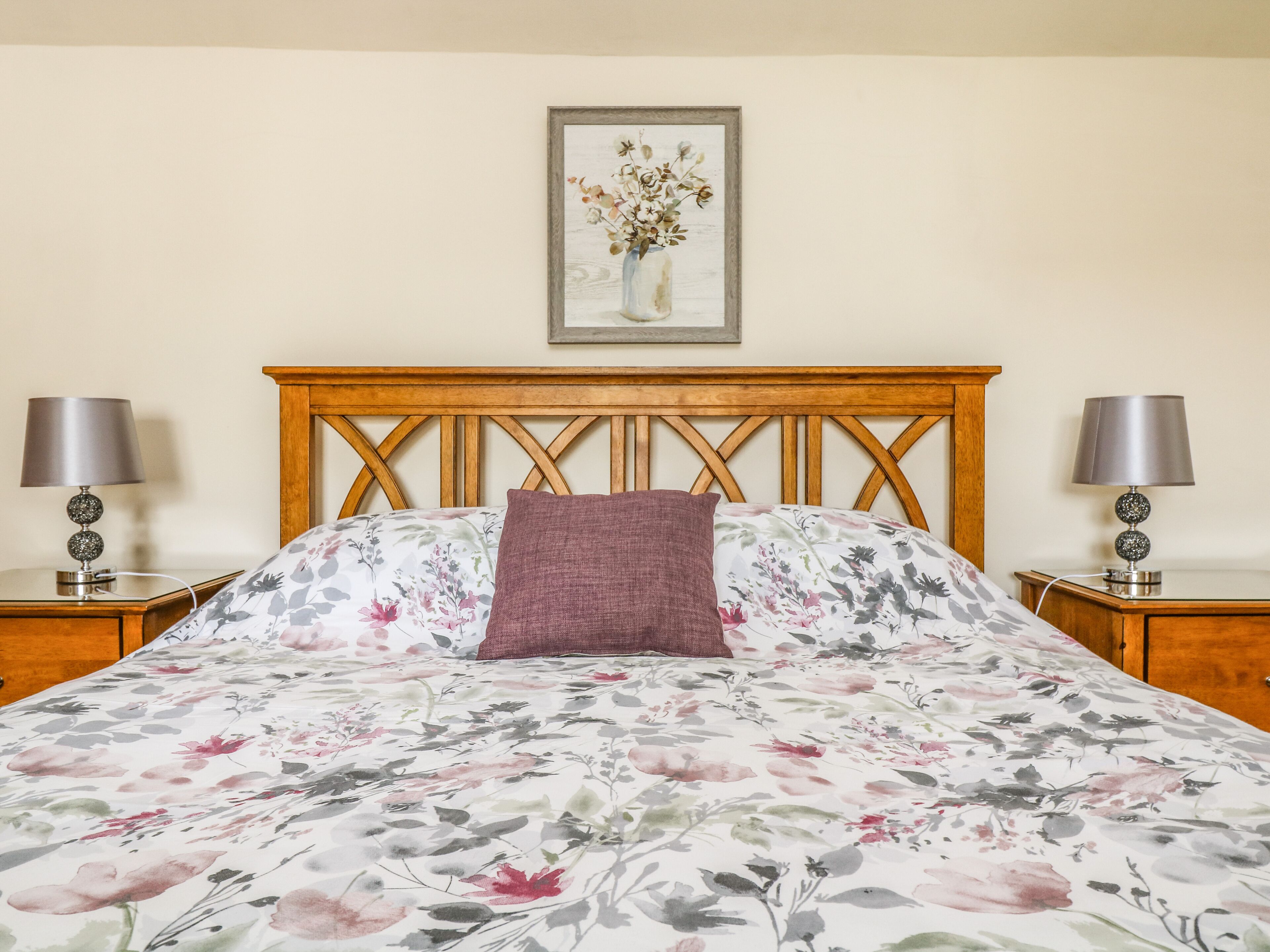 A neatly made bed with floral bedding, a wooden headboard, and two bedside lamps.