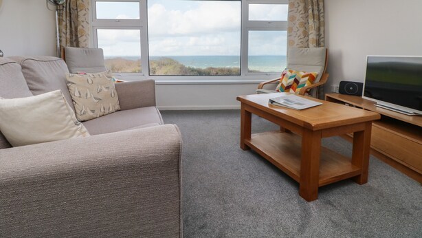 Un salon chaleureux avec un canapé, une table basse en bois, un téléviseur et une vue sur la mer.