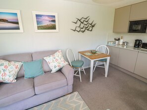 A living room with a sofa, a table with chairs, a kitchen area, and two framed pictures on the wall.
