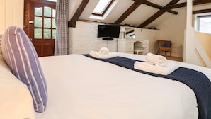 A bedroom with a large bed, a wooden ceiling, a television, a dresser, and a window.