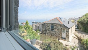 A stone house with a red roof, a small garden, and a view of the sea. - Rose Villa (Penzance)