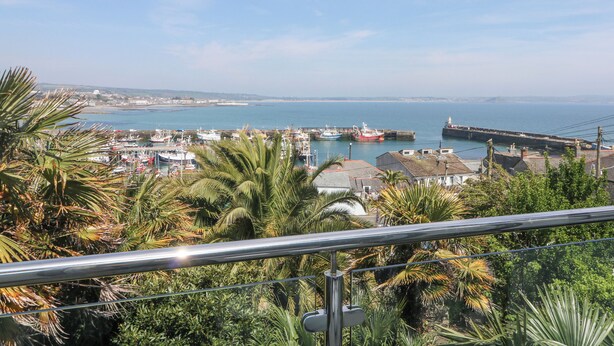 A coastal town with a marina, boats, and a lighthouse in the distance. - Rose Villa (Penzance)