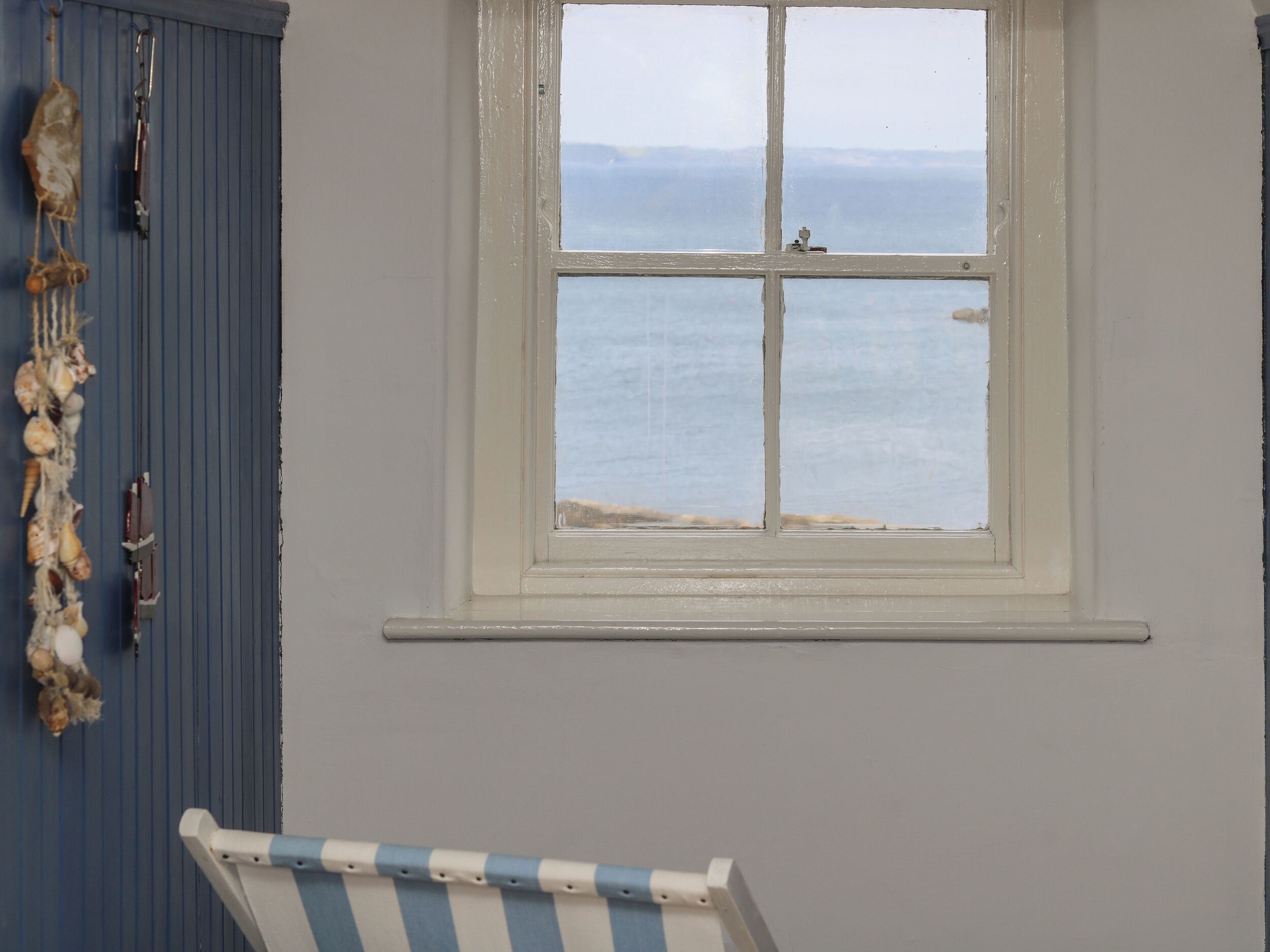 A room with a window overlooking the sea, a blue wall, and a striped chair.