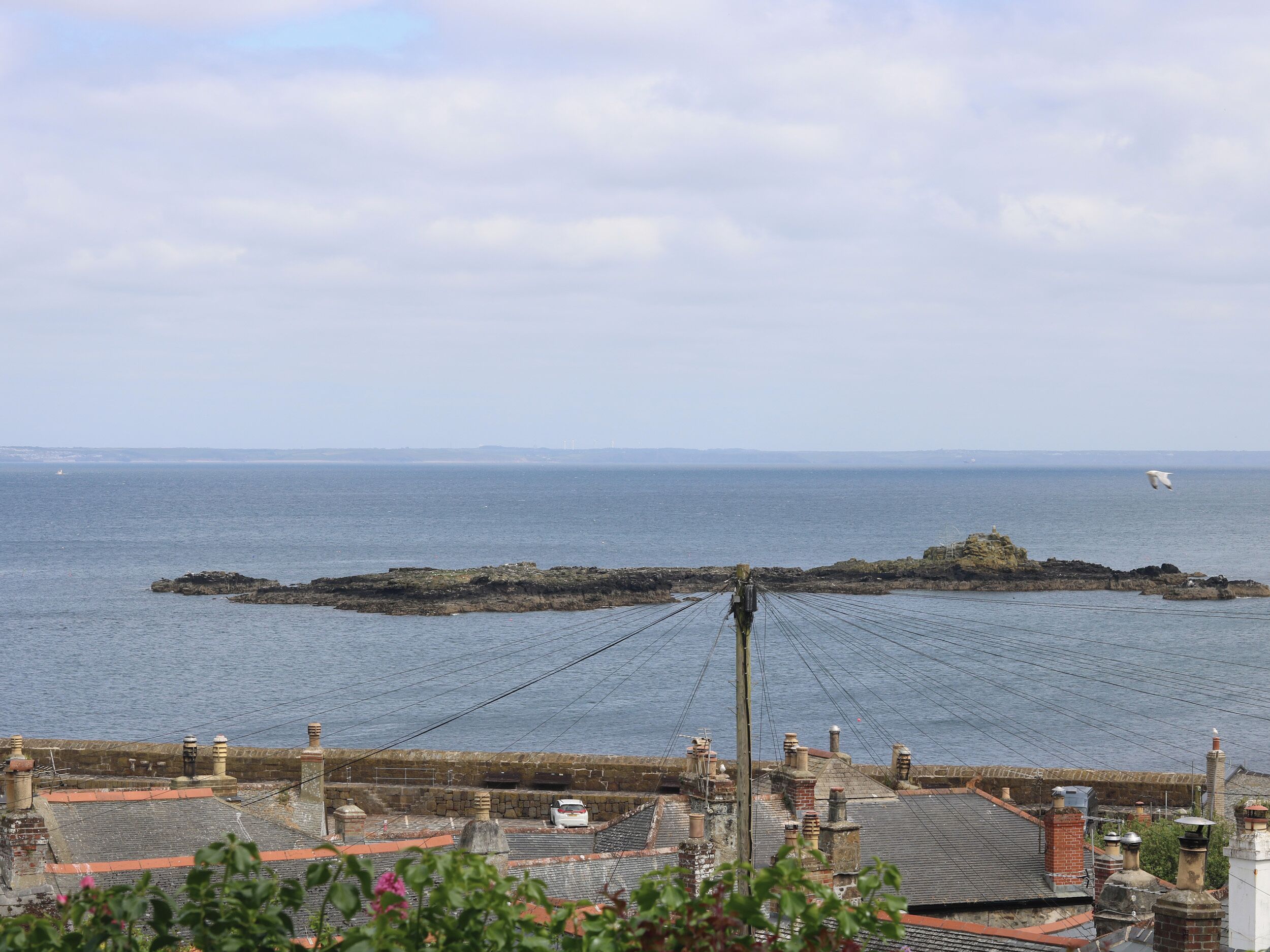 Une vue côtière avec un promontoire rocheux dans la mer, un pont et des bâtiments aux toits recouverts de tuiles rouges.