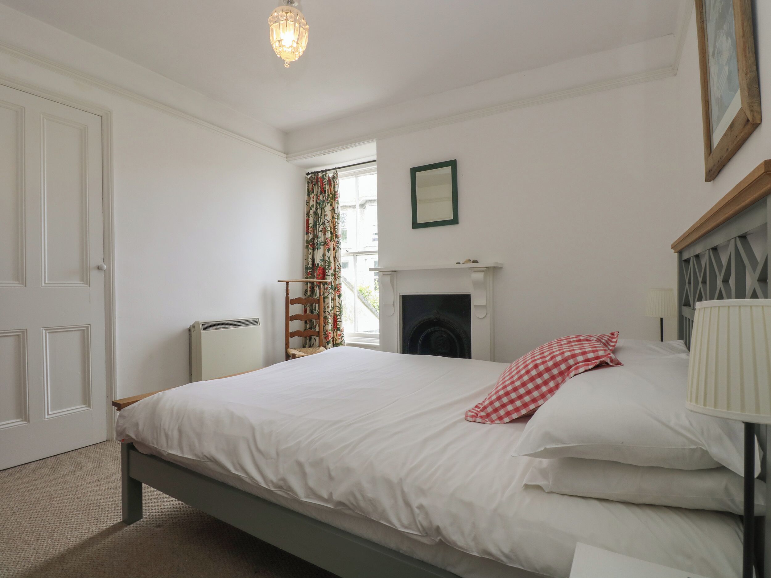 A bedroom with a bed, a fireplace, a window with curtains, and a door.