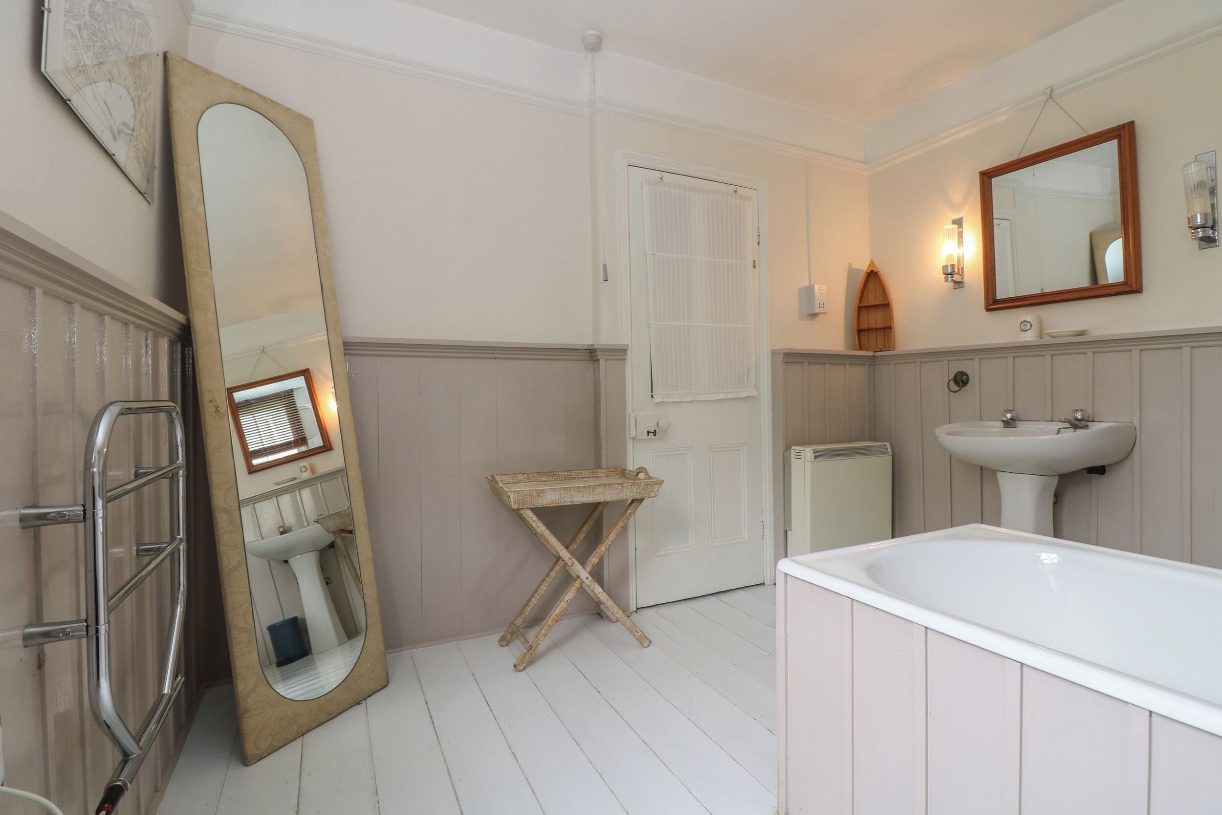 A bathroom with a large mirror, a bathtub, a sink, and a door.