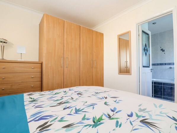 A bedroom with a wooden wardrobe, a bed with a floral bedspread, and a bathroom visible through an open door.