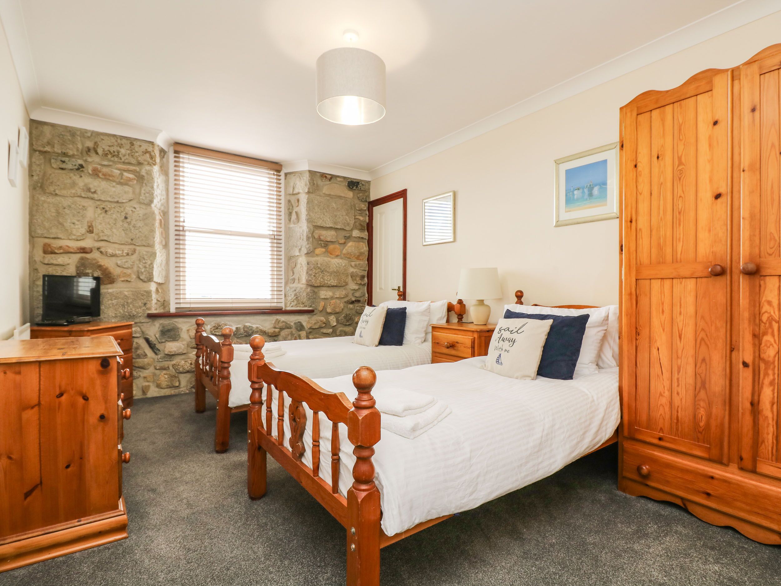 A bedroom with two wooden beds, a stone wall, a wooden wardrobe, and a television on a dresser.