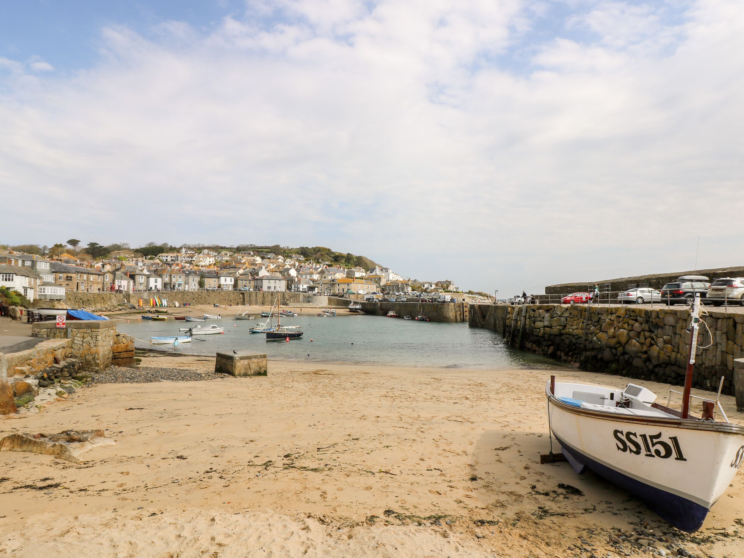 A sandy beach with a boat named SS151, a stone wall, and a town in the background.