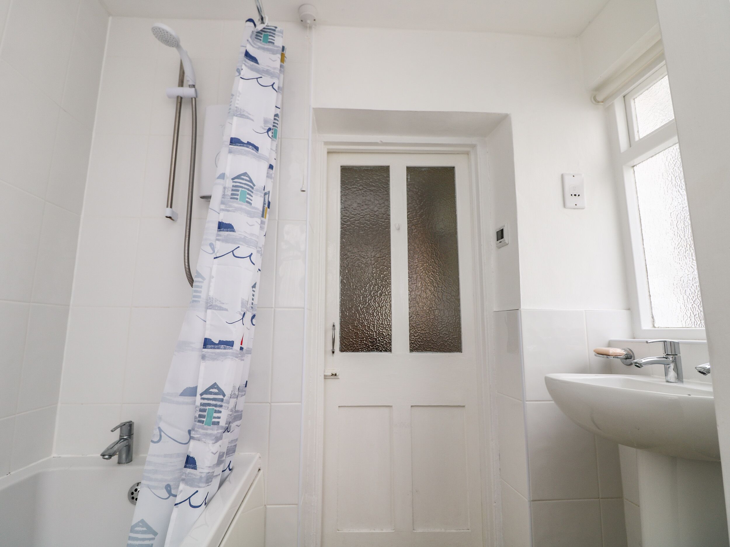 A bathroom with a bathtub, a shower curtain, a door with frosted glass panels, and a sink with a soap dish.