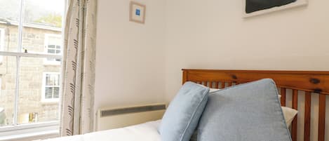 A bedroom with a wooden headboard, white bedding, and a window with curtains.