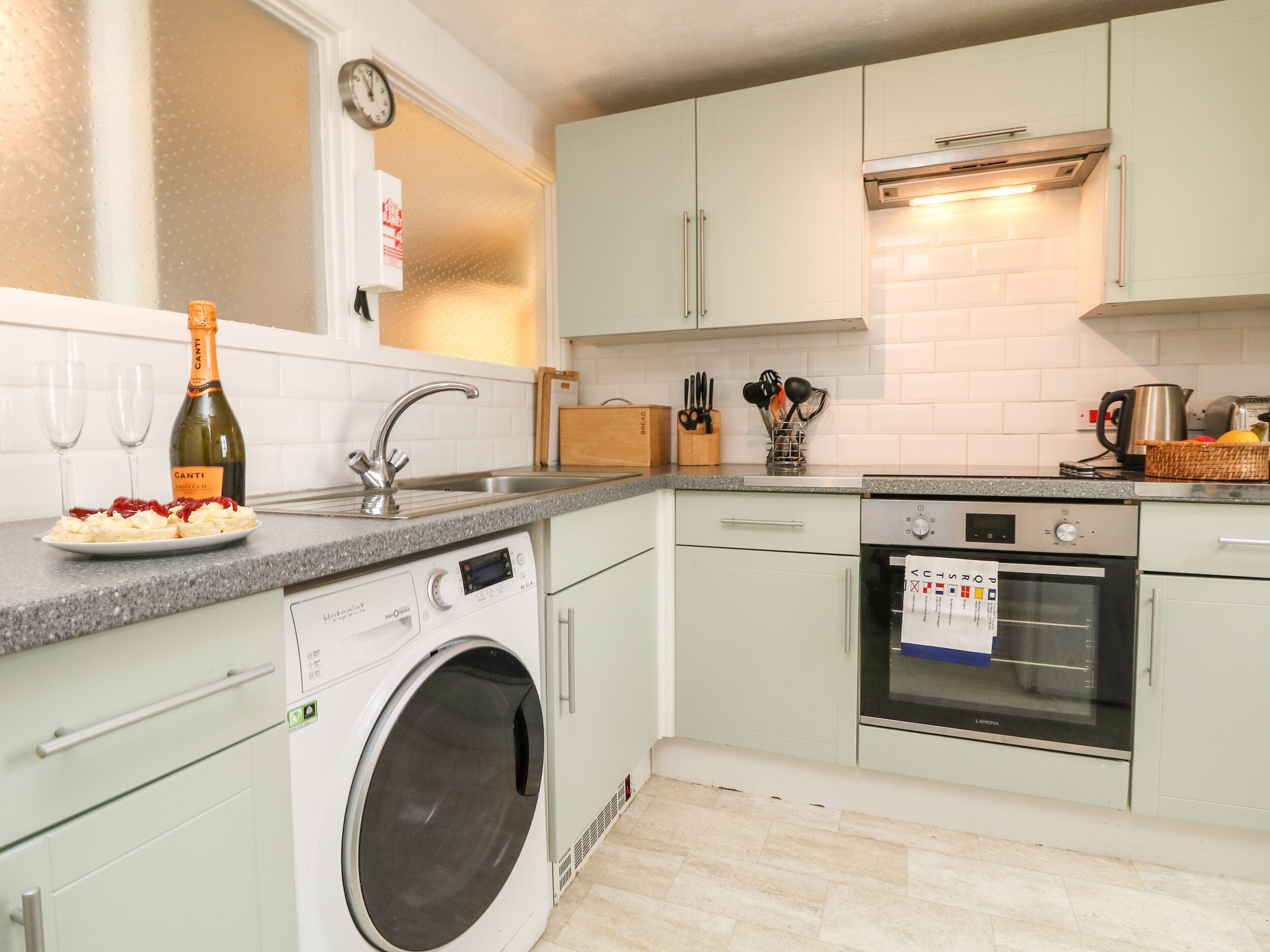 A modern kitchen with a washing machine, oven, and a bottle of Canti wine.