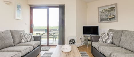 Ein modernes Wohnzimmer mit zwei grauen Sofas, einem Holztisch, einem Fernseher und einem großen Fenster mit Blick auf Boote.