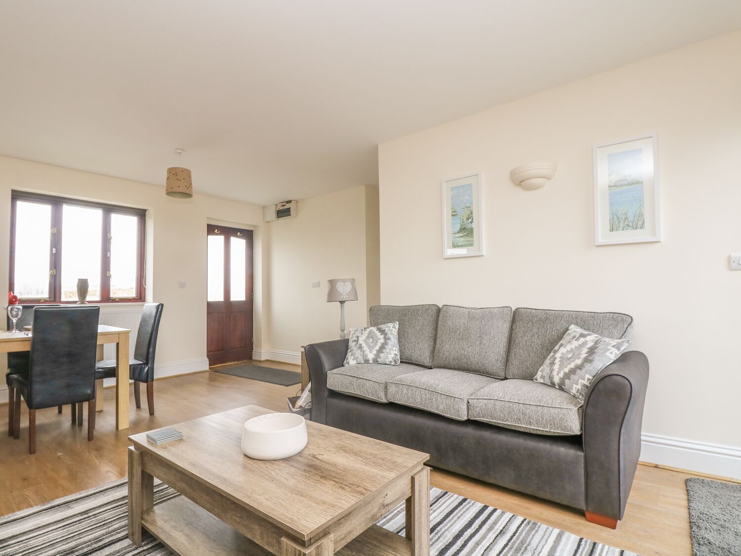 Ein Wohnzimmer mit grauem Sofa, einem Holztisch und einem Essbereich mit Tisch und Stühlen.