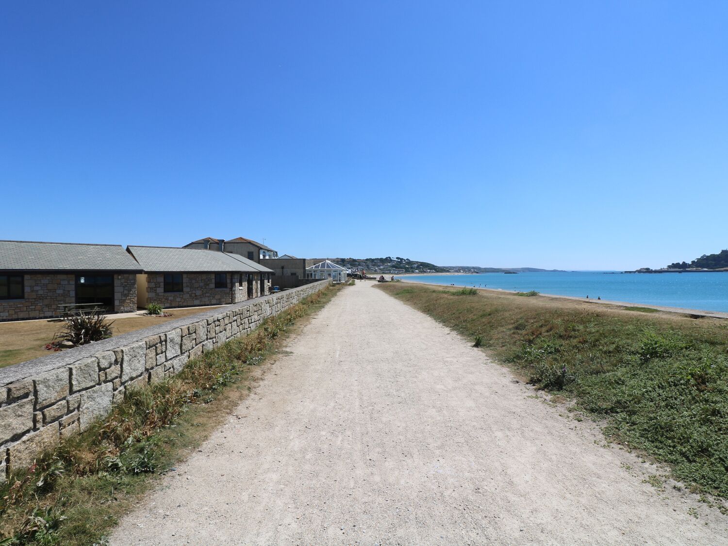 A coastal road leading to a beach with stone buildings and a clear blue sky.