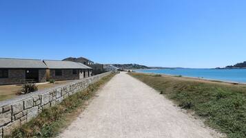 A coastal road leading to a beach with stone buildings and a clear blue sky.