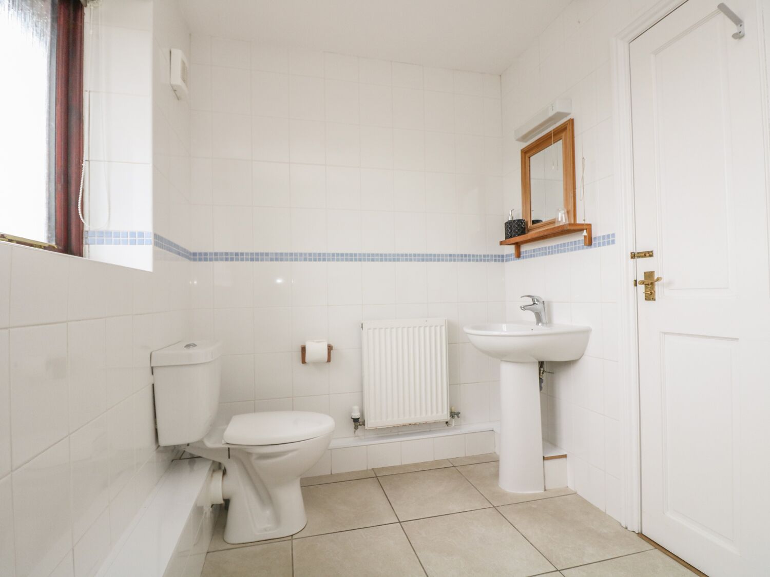 Un baño pequeño y limpio, con azulejos blancos, un inodoro, un lavamanos y un espejo.