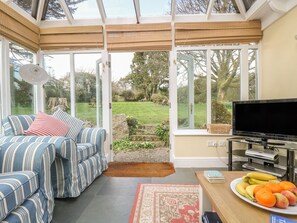 A conservatory with a sofa, TV, and fruit on a table.