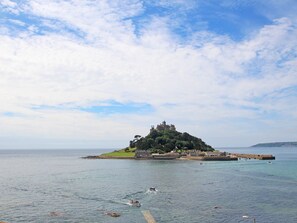 Vista costera con un castillo histórico en una pequeña isla, rodeada de aguas tranquilas y un cielo despejado.