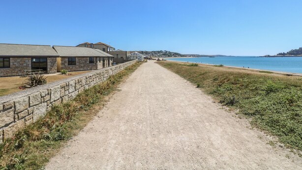 A coastal path leading to a beach with stone buildings and a clear blue sky. - Shoreline (Penzance)