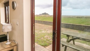 A room with a wooden door leading to a grassy area, a clock on the wall, and a wooden table outside. - Shoreline (Penzance)