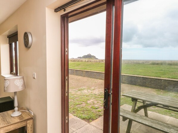A room with a wooden door leading to a grassy area, a clock on the wall, and a wooden table outside. - Shoreline (Penzance)