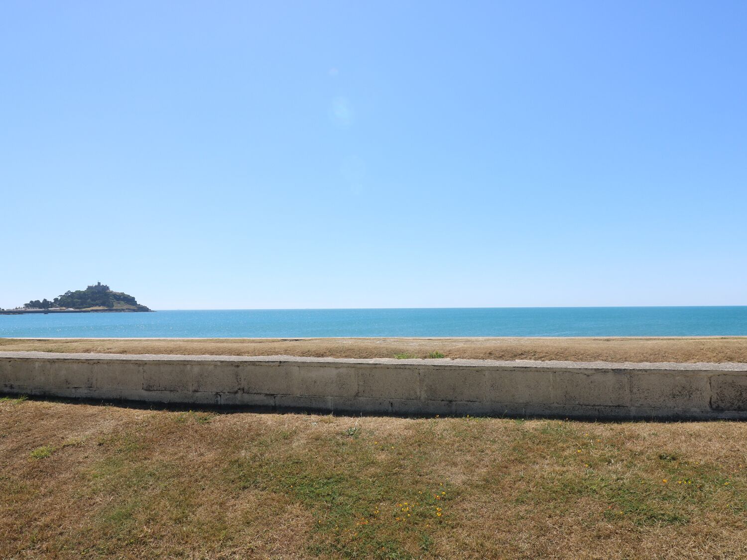 A coastal view with a grassy area in the foreground and a small island with a structure in the distance.