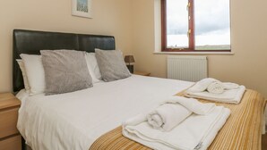 A neatly made bed with white linens and two rolled towels on a striped bedspread. - Shoreline (Penzance)