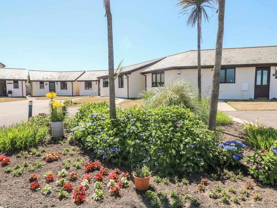 A row of single-story buildings with a flat roof, surrounded by a landscaped garden with various plants and flowers.