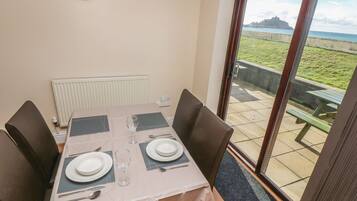 A dining area with a table set for two, a view of the sea through a glass door, and a white radiator on the wall.