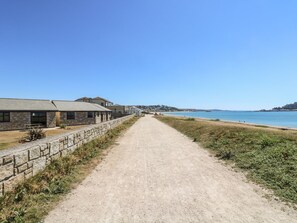 A coastal path leading to a beach with stone buildings and a clear blue sky. - Seabreeze (Penzance)
